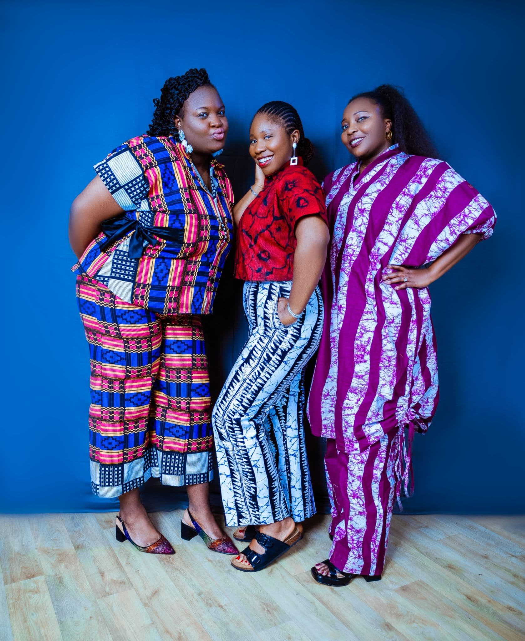 Three women wearing Ankara outfits against a blue backdrop