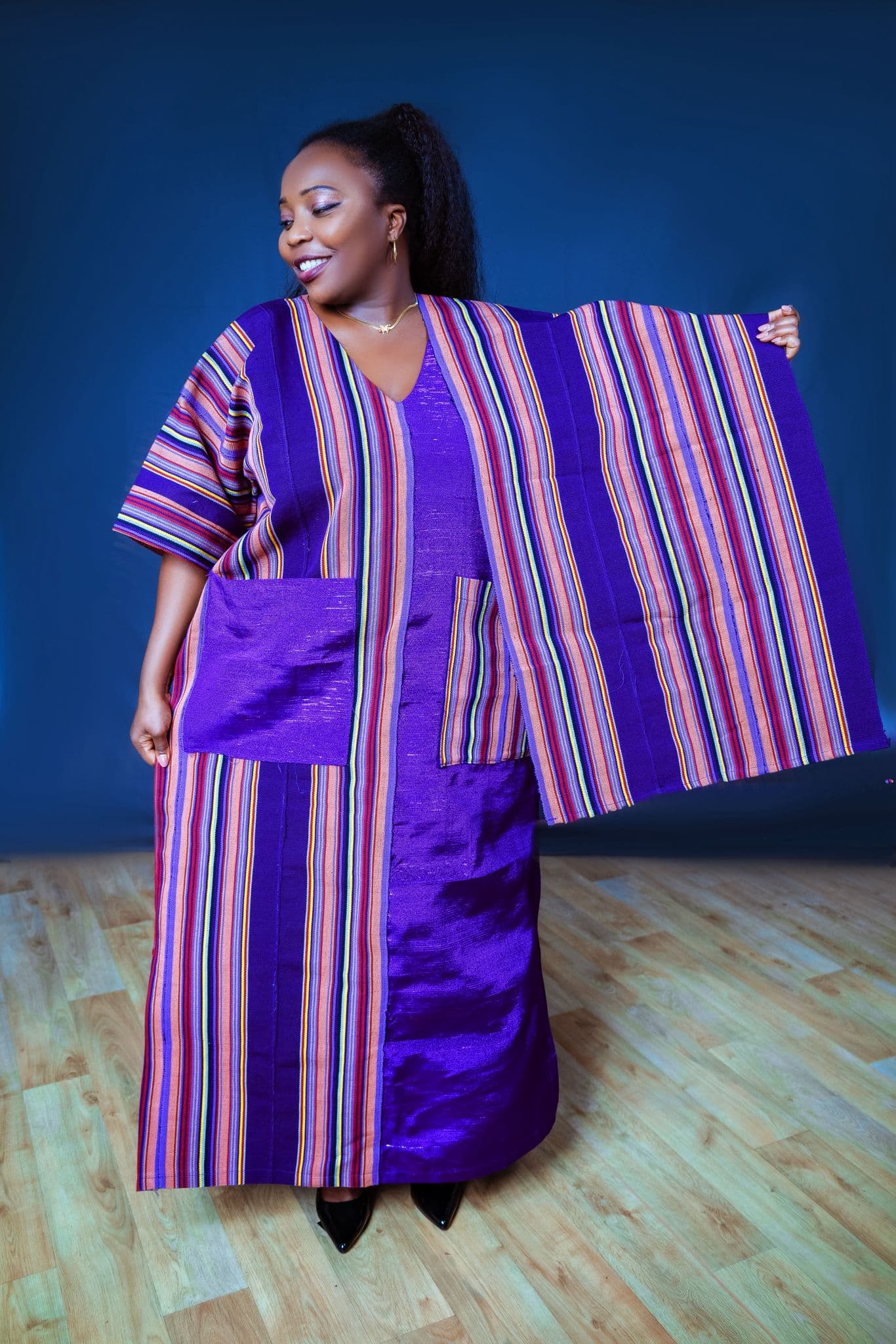 Woman presenting a purple striped Ankara outfit against a blue backdrop