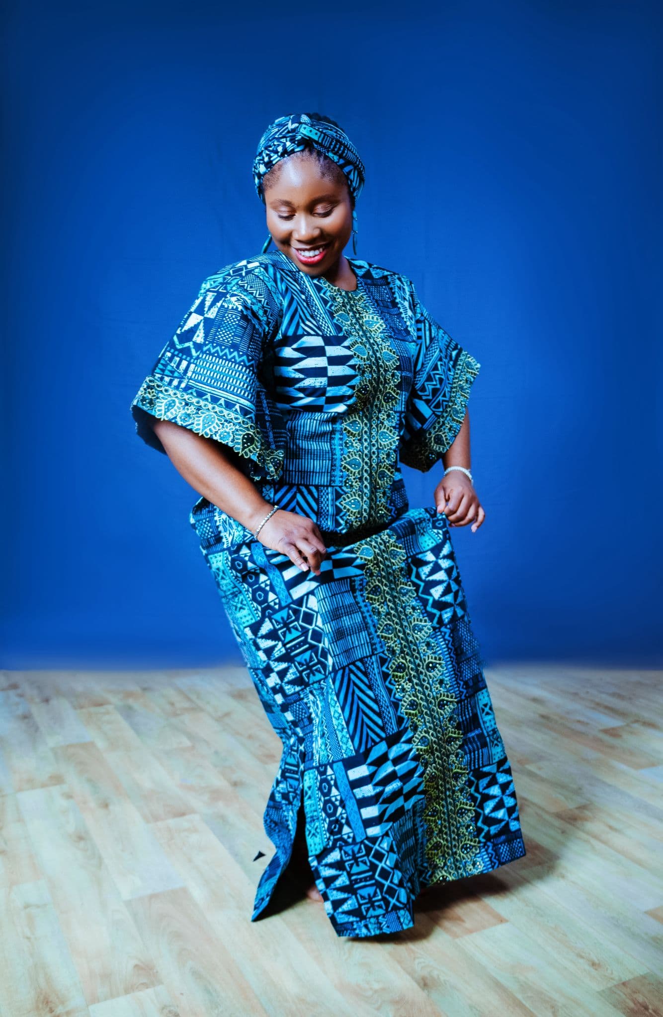 Two women in Ankara outfits posing together against a blue backdrop